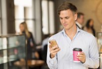 Uomo con caffè da asporto tramite smartphone — Foto stock