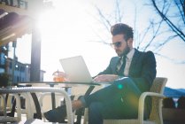 Jovem empresário elegante usando laptop no café da calçada — Fotografia de Stock