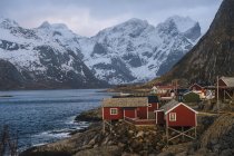 Edificios del pueblo de pescadores en la orilla con montañas nevadas - foto de stock