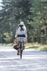 Rear view of woman cycling on forest road with foraging baskets — Stock Photo