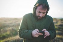 Hombre adulto medio usando smartphone mientras mastica cerillas en el campo - foto de stock