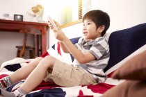 Jeune garçon assis sur le canapé regardant la télévision à la maison — Photo de stock