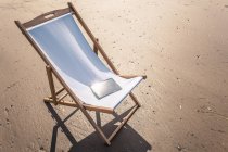 Chaise longue sur la plage avec livre électronique sur le siège — Photo de stock