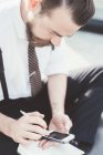 Бізнесмен сидить хрест ногами роблячи щоденник нотатки зі смартфона за межами офісу — стокове фото