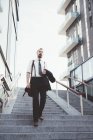 Businessman carrying jacket moving down city stairway — Stock Photo