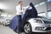 Salesman uncovering new car in car dealership — Stock Photo