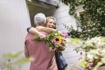 Esposa sosteniendo ramo de flores y abrazando marido - foto de stock