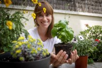 Mulher adulta média segurando planta manjericão em mãos de xícara, sorrindo para a câmera — Fotografia de Stock