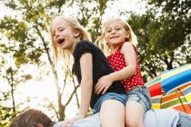 Mature man giving two young daughters piggy back in park — Stock Photo