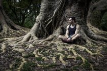 Joven sentado en las raíces de los árboles del parque, Sao Paulo, Brasil - foto de stock