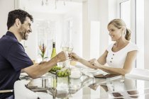 Couple d'âge mûr assis à table, tenant des verres à vin, portant un toast — Photo de stock