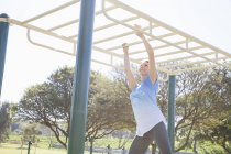 Mittlere erwachsene Frau trainiert im Park an Affenstangen — Stockfoto