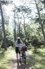 Зрелая женщина толкает велосипед с корзинами на лесной дорожке — стоковое фото