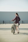 Молода жінка озирається назад, штовхаючи велосипед на порожній парковці — стокове фото