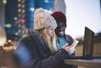 Couple using smartphone and laptop outdoors at dusk — Stock Photo