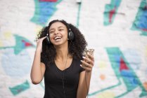 Teenager listening to mp3 player against wall with graffiti — Stock Photo