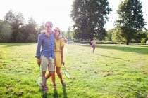 Романтическая молодая пара с ракетками для бадминтона в солнечном парке — стоковое фото