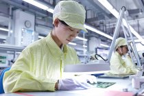 Young woman working at quality check station at factory producing flexible electronic circuit boards. Plant is located in the south of China, in Zhuhai, Guangdong province — Stock Photo