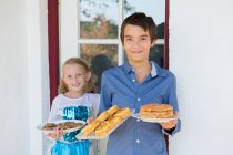 Portrait of teenage boy and sister carrying cakes on patio — Stock Photo