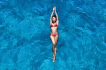 Young woman in red bikini floating in blue sea water, high angle — Stock Photo