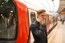 Empresario que usa teléfono en la plataforma, estación de metro, Londres, Reino Unido - foto de stock