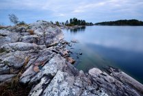 Scenic view of rocky shore and still lake under cloudy sky — Stock Photo