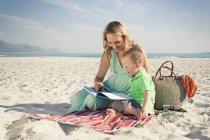 Mid adult mother reading with little son on beach, Cape Town (Cidade Do Cabo), Western Cape, África do Sul — Fotografia de Stock