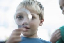 Portrait of boy holding magnifying glass in front of eye — Stock Photo