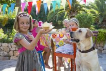 Girl at birthday party with dog holding cupcake — Stock Photo