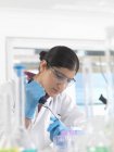 Jeune femme scientifique pipettant un échantillon dans un flacon dans un laboratoire utilisé pour les tests chimiques et ADN — Photo de stock