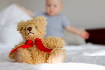Cute teddy bear sitting up in bed in front of baby girl — Stock Photo