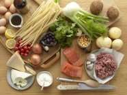 Alimentos crudos frescos con huevos, pasta, hierbas, queso, verduras, salmón y cerdo picado - foto de stock
