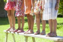 Обрезанный снимок ног пяти девушек, стоящих на скамейке в саду — стоковое фото