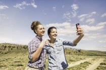 Dos mujeres jóvenes tomando smartphone selfie en la pista de tierra, Bridger, Montana, Usa. - foto de stock