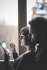 Casal em pé ao lado da janela, usando tablet digital — Fotografia de Stock