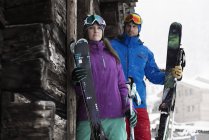 Man and woman outside chalet holding skis — Stock Photo