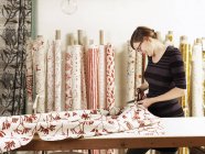 Woman cutting fabric on work table in hand-printed textile workshop — Stock Photo