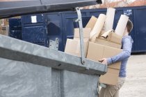 Мальчик-подросток несет картонные отходы в мусорное ведро — стоковое фото