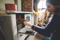 Side view of young woman putting firewood into wood burner — Stock Photo