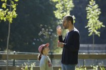 Man blowing bubbles as daughter looks up — Stock Photo