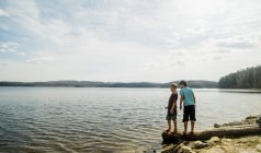 Two boys standing on fallen tree looking down into lake — Stock Photo