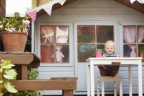 Baby girl sitting at table in front of playhouse looking at camera smiling — Stock Photo