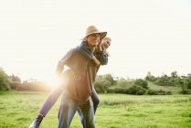 Young man giving girlfriend a piggyback in rural field — Stock Photo