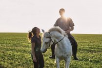 Woman chatting with man riding grey horse in field — Stock Photo