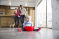 Famille regardant mâle tout-petit avec bol sur le sol de la salle à manger — Photo de stock