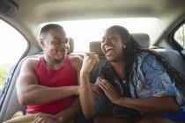 Young couple in car laughing, woman flexing muscles — Stock Photo