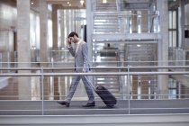 Young businessman with wheeled case on conference centre walkway — Stock Photo