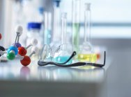 Óculos de segurança e modelo molecular em bancada de laboratório, equipamentos científicos em segundo plano — Fotografia de Stock