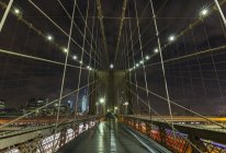 Passerella del ponte di Brooklyn e distante skyline del distretto finanziario di Manhattan di notte, New York, USA — Foto stock