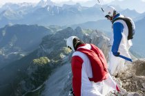 Two male BASE jumpers standing on edge of mountain looking down, Dolomites, Italy — Stock Photo